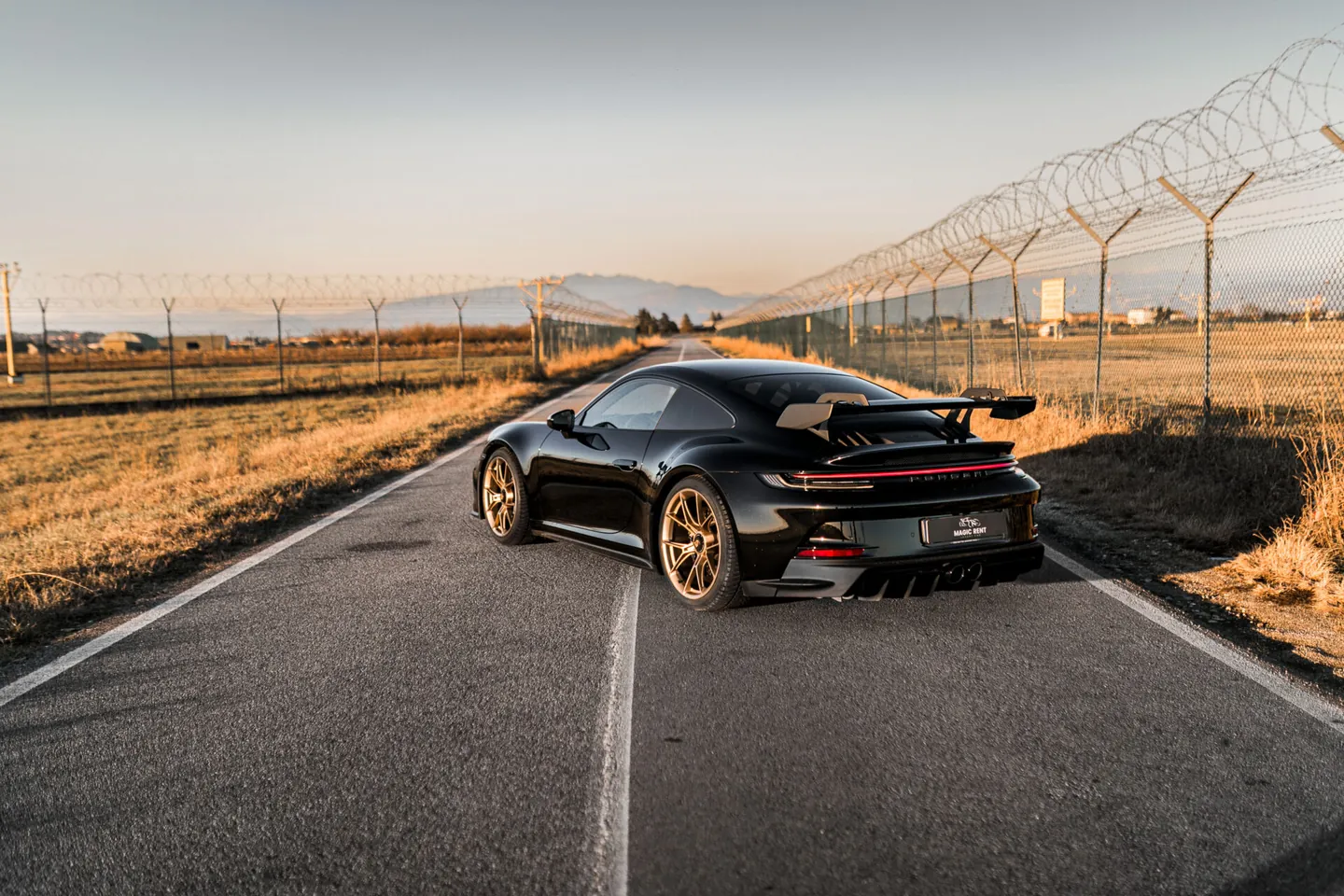 Porsche nera vista da dietro, al centro di una strada di campagna