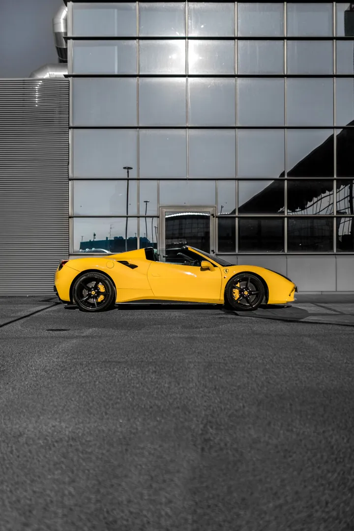 Ferrari gialla scoperta di profilo, davanti a un edificio di vetro